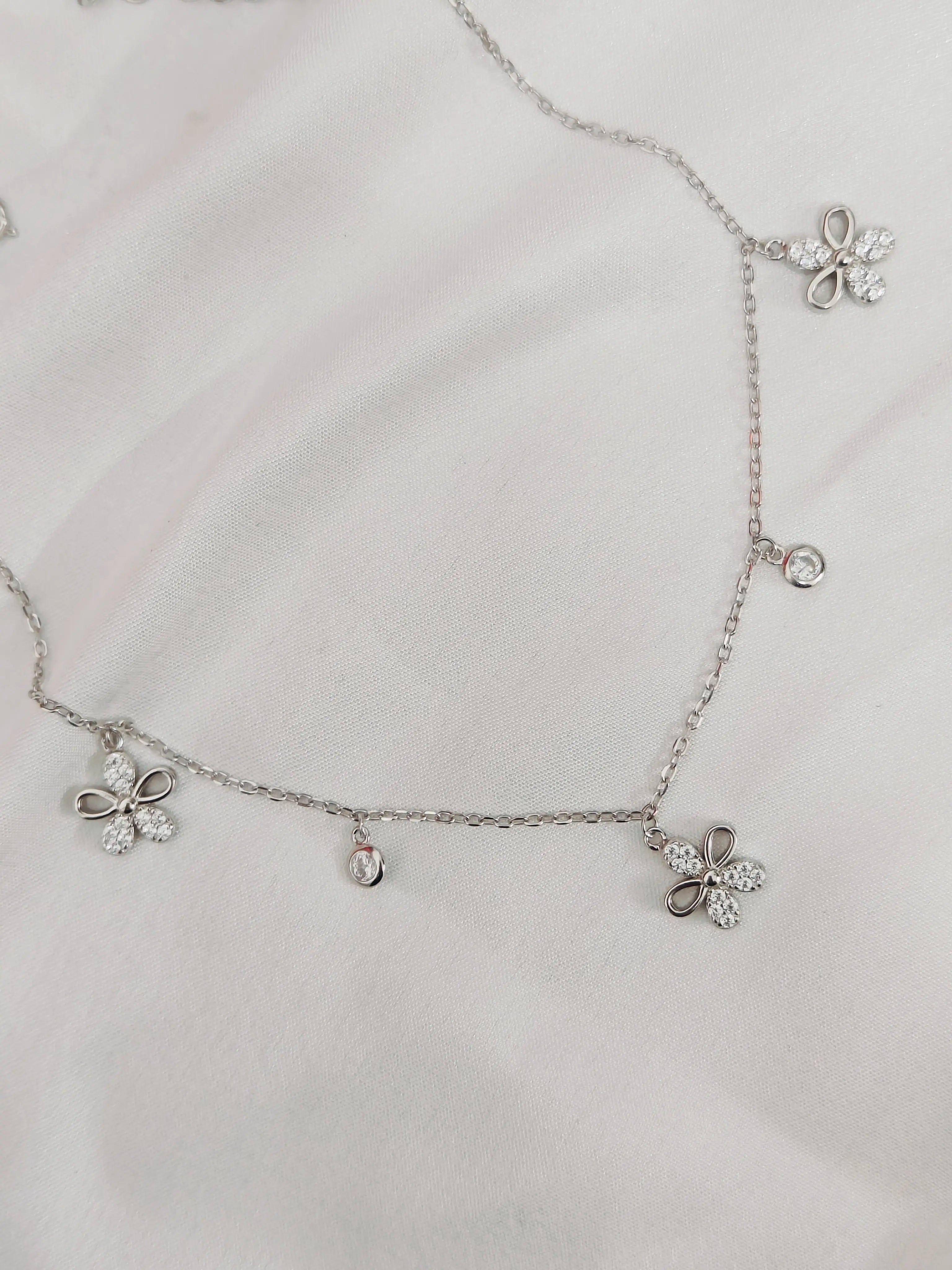 Silver necklace with floral pendants on a light gray background